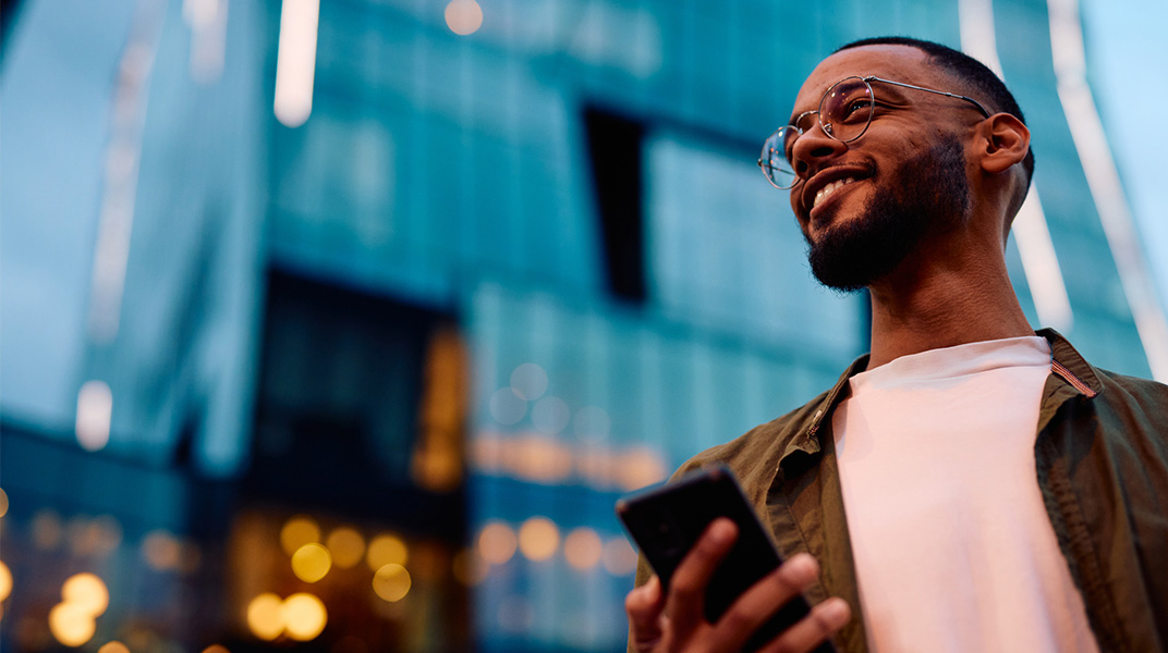 Professional using a mobile device in a modern urban business district, representing fast-moving consulting work supported by global mobility programs.